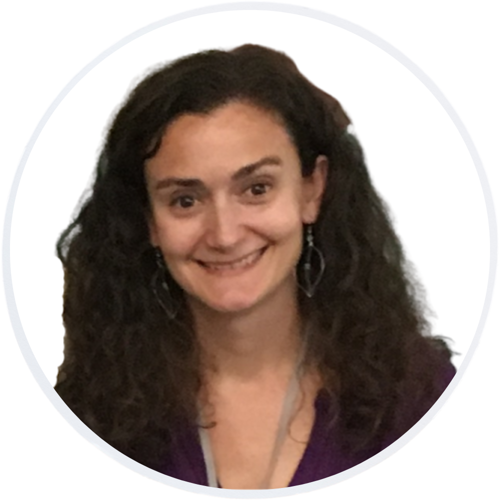 A woman with long, curly brown hair, wearing a purple top and dangling earrings, smiles at the camera. She is pictured inside a circular frame with a white background.